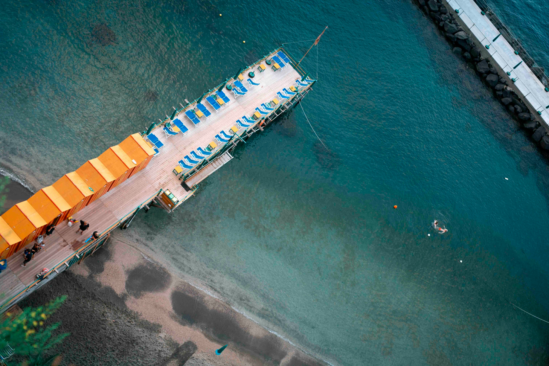 Aerial view of an orange-cabana pier over turquoise water on the Sorrento coast
