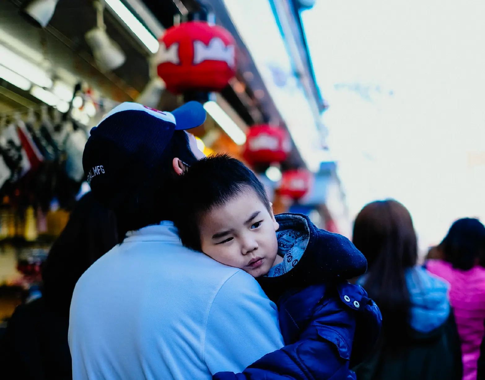Child resting on his father's shoulder beneath red lanterns