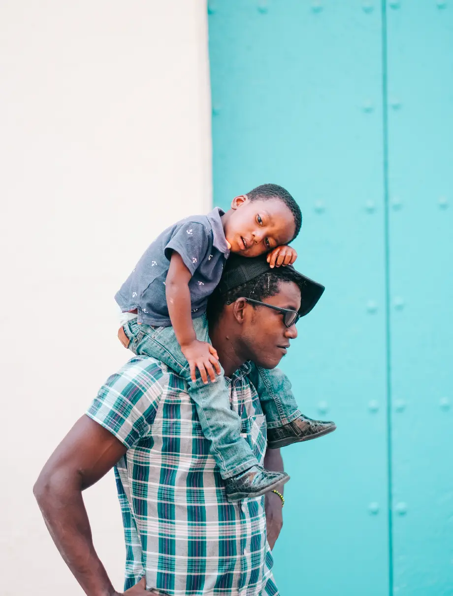 Father carrying his son on his shoulders against a turquoise door