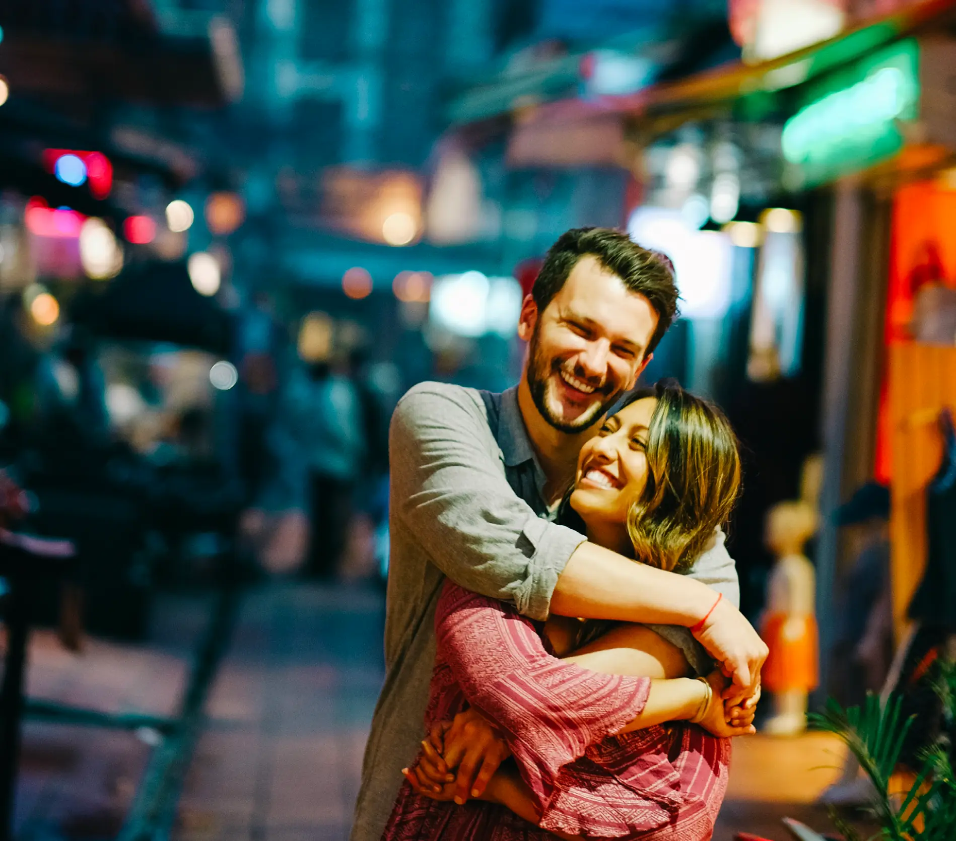 Couple laughing in an embrace on a neon-lit street at night