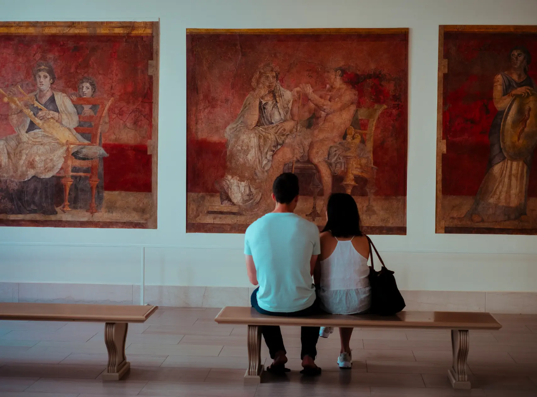 Couple sitting on a bench before red Roman frescoes in a gallery