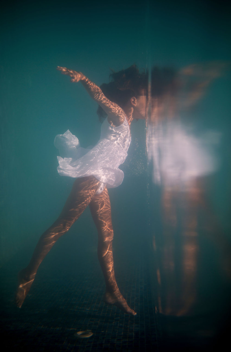 Dancer in white lace suspended against a teal pool wall