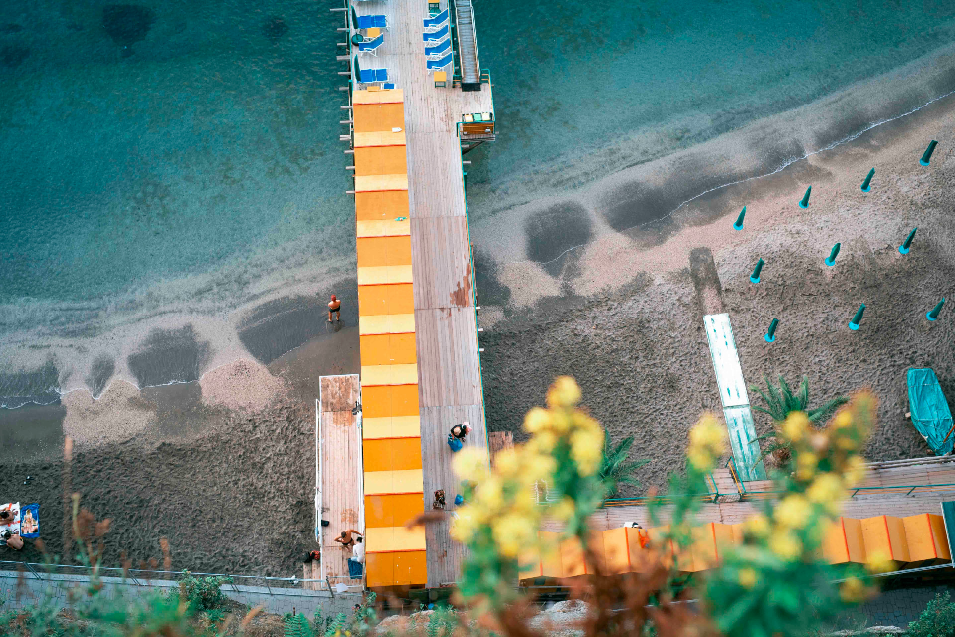 Aerial view of an orange boardwalk crossing a grey pebble beach in Italy