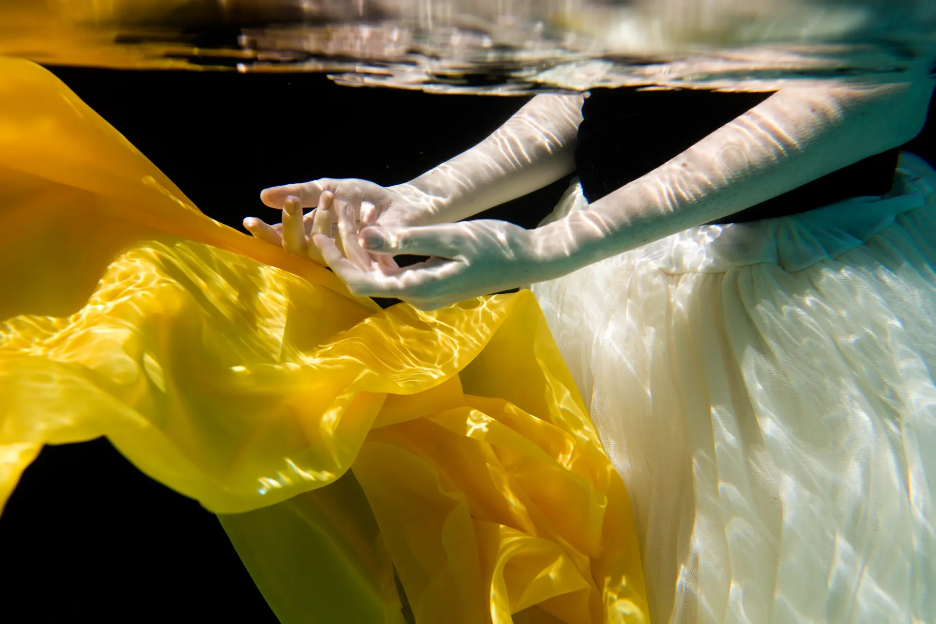 Hands meeting underwater between yellow and white silk skirts