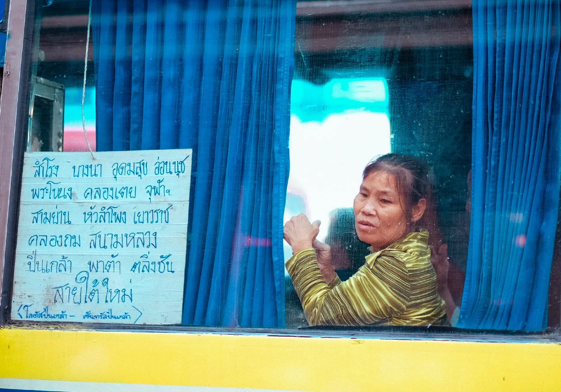 Woman leaning from the blue-curtained window of a Bangkok bus