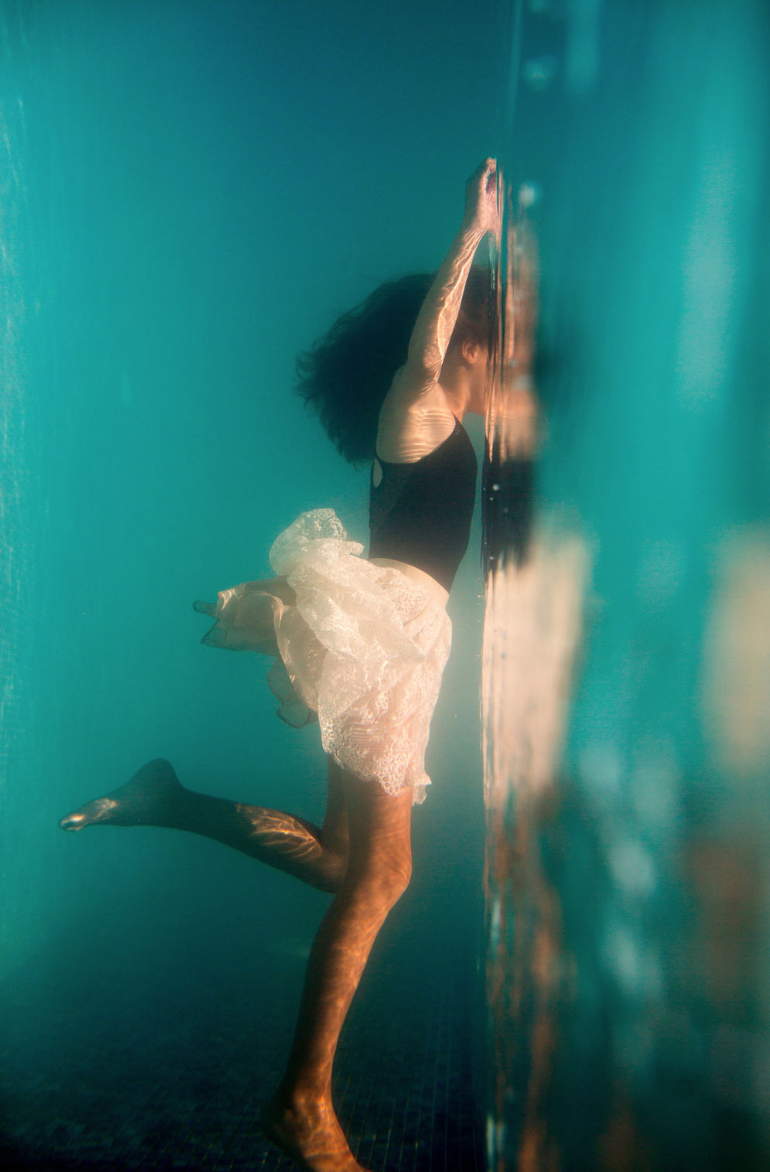 Dancer reaching upward underwater, skirt blooming around her