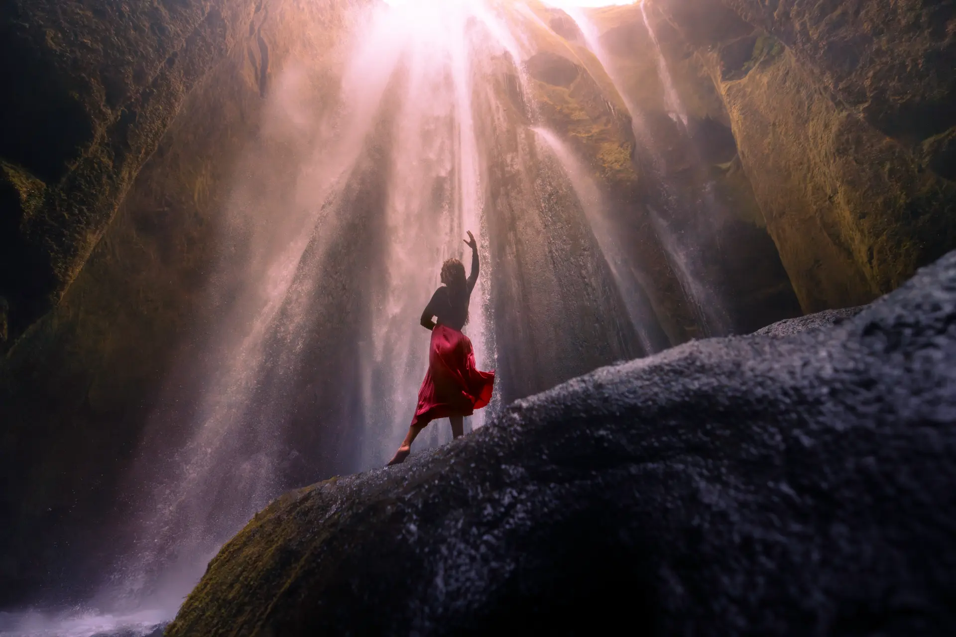 Woman in a red silk skirt in the light beams of Gljúfrabúi waterfall