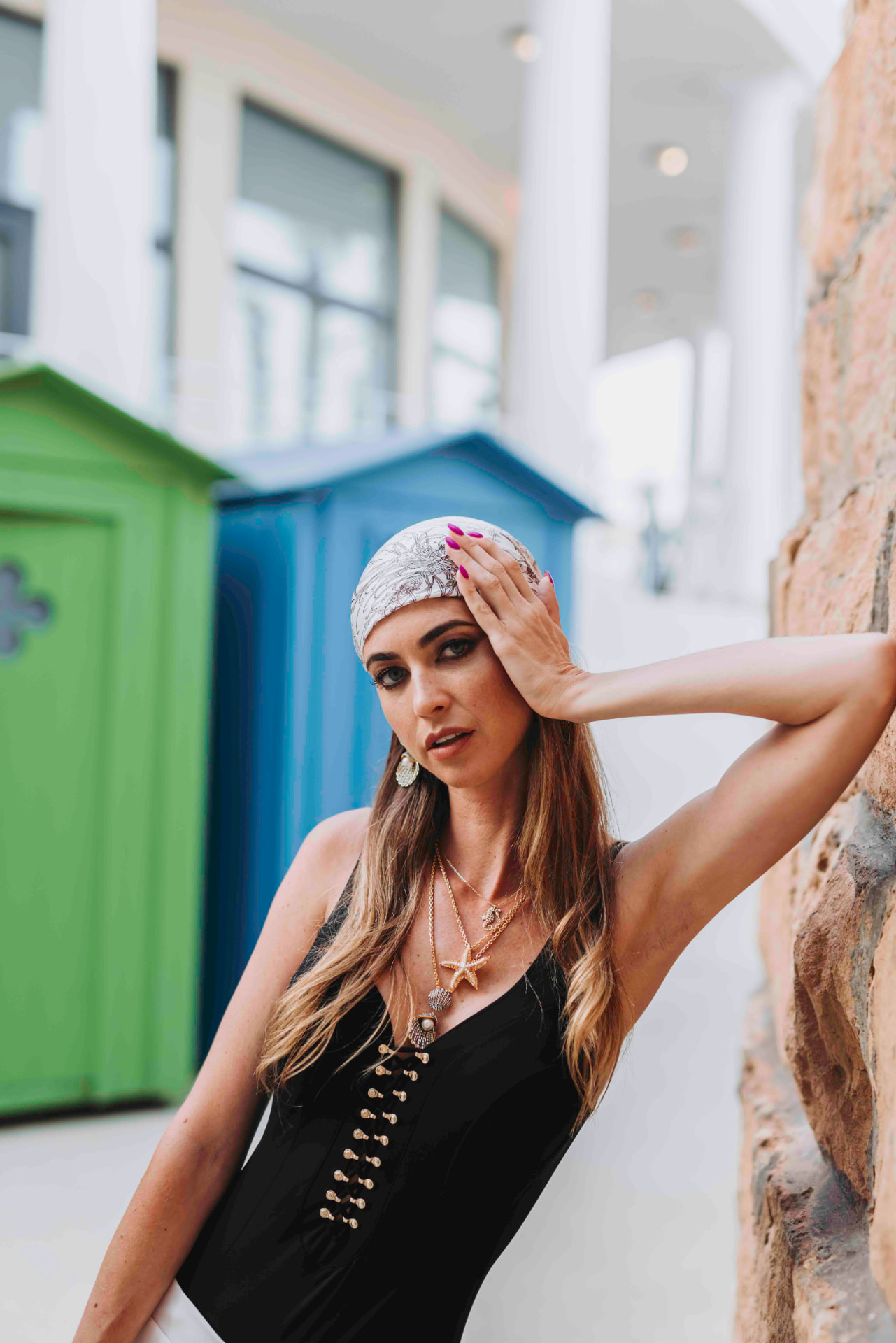 Model in a black lace-up swimsuit and shell jewellery by painted beach huts