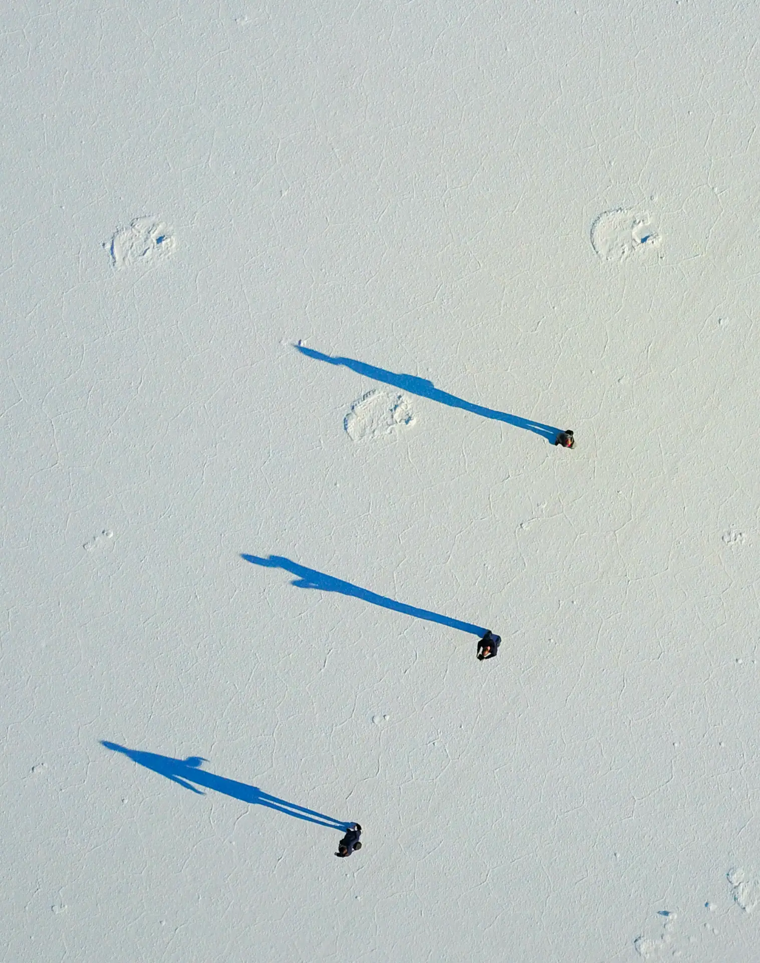 Aerial view of three figures casting long blue shadows on the Uyuni salt flats