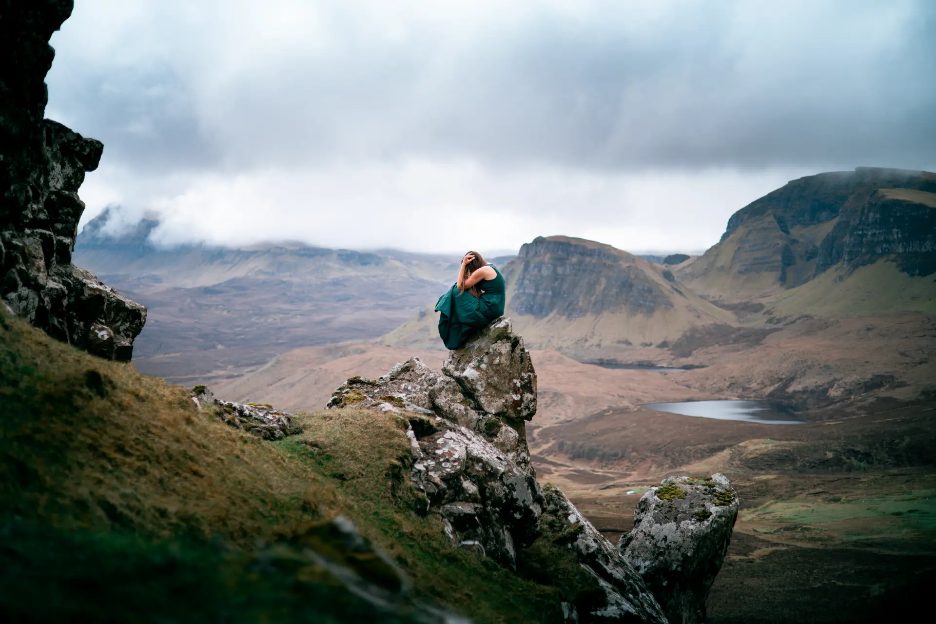 Woman in a green dress seated on a rock above the Quiraing highlands