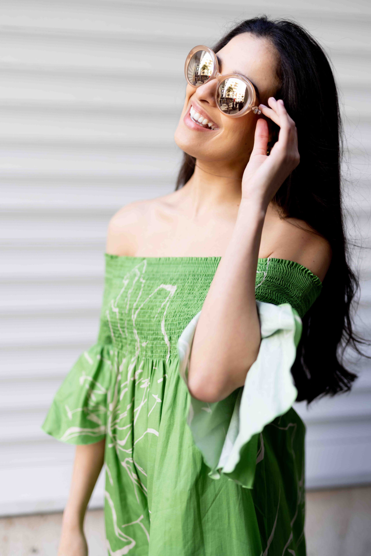 Model in a green off-shoulder dress and round sunglasses smiling