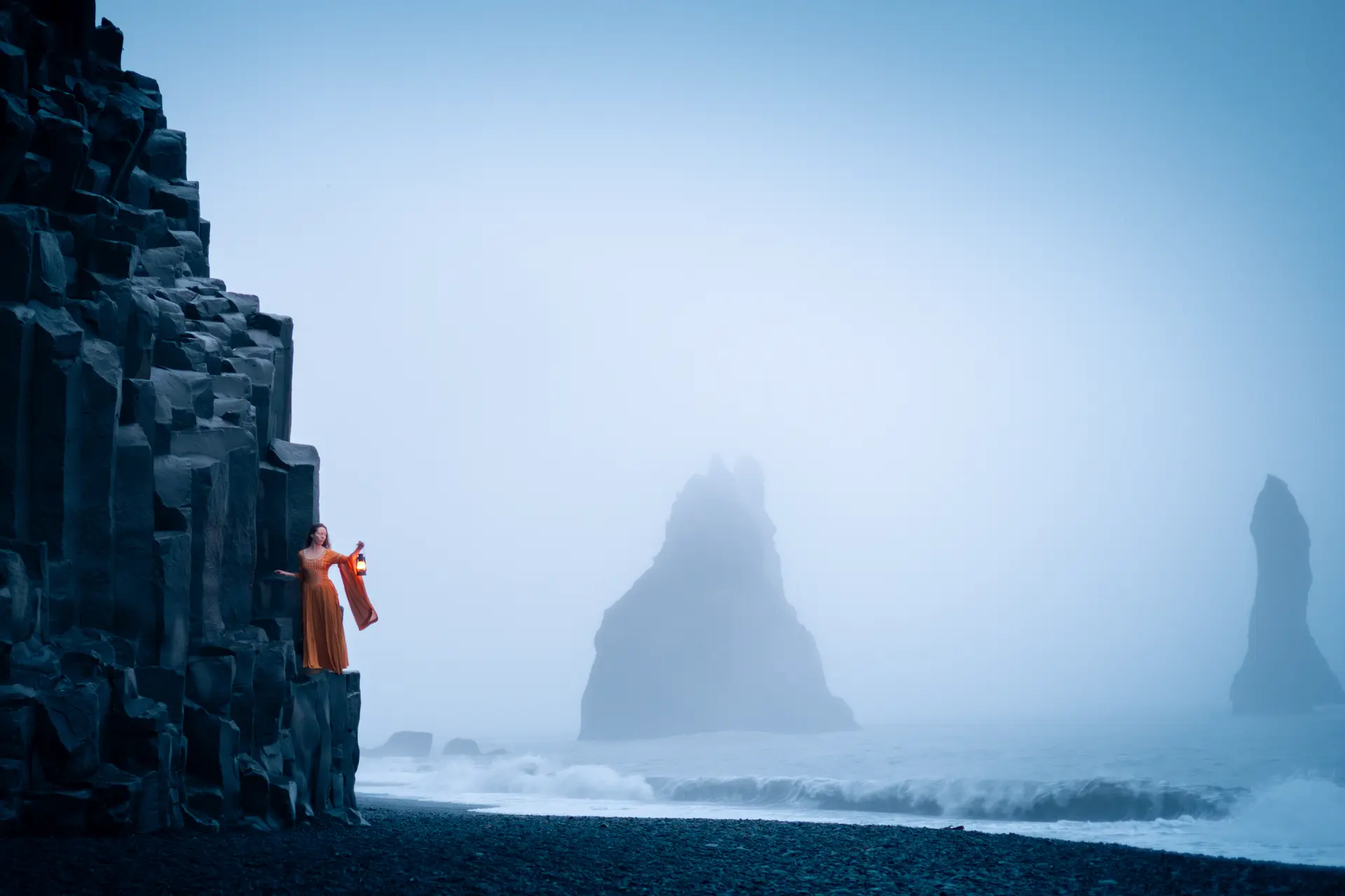 Woman holding a lantern on the basalt columns at Reynisfjara