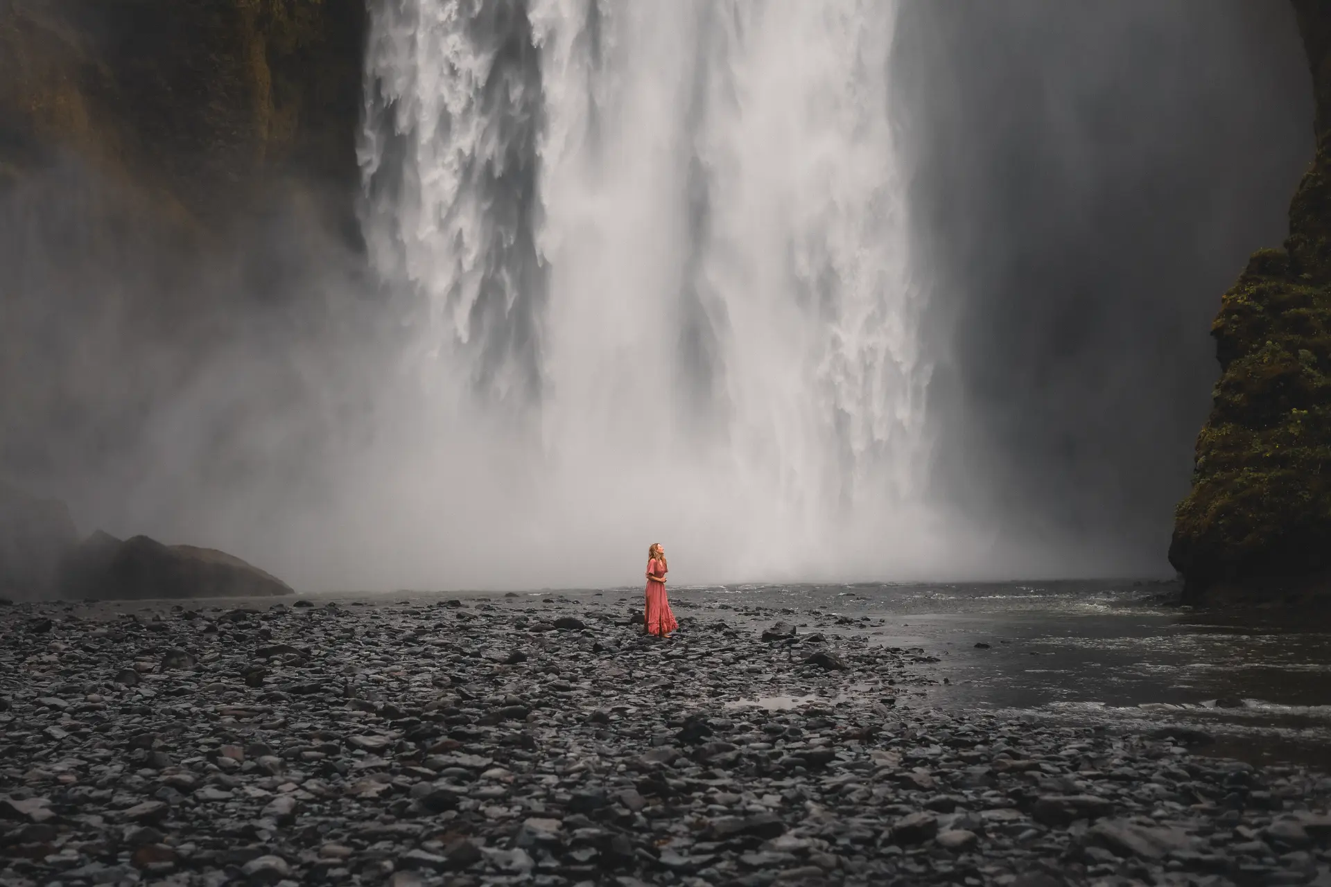 Woman in a coral dress beneath the falls at Skógafoss