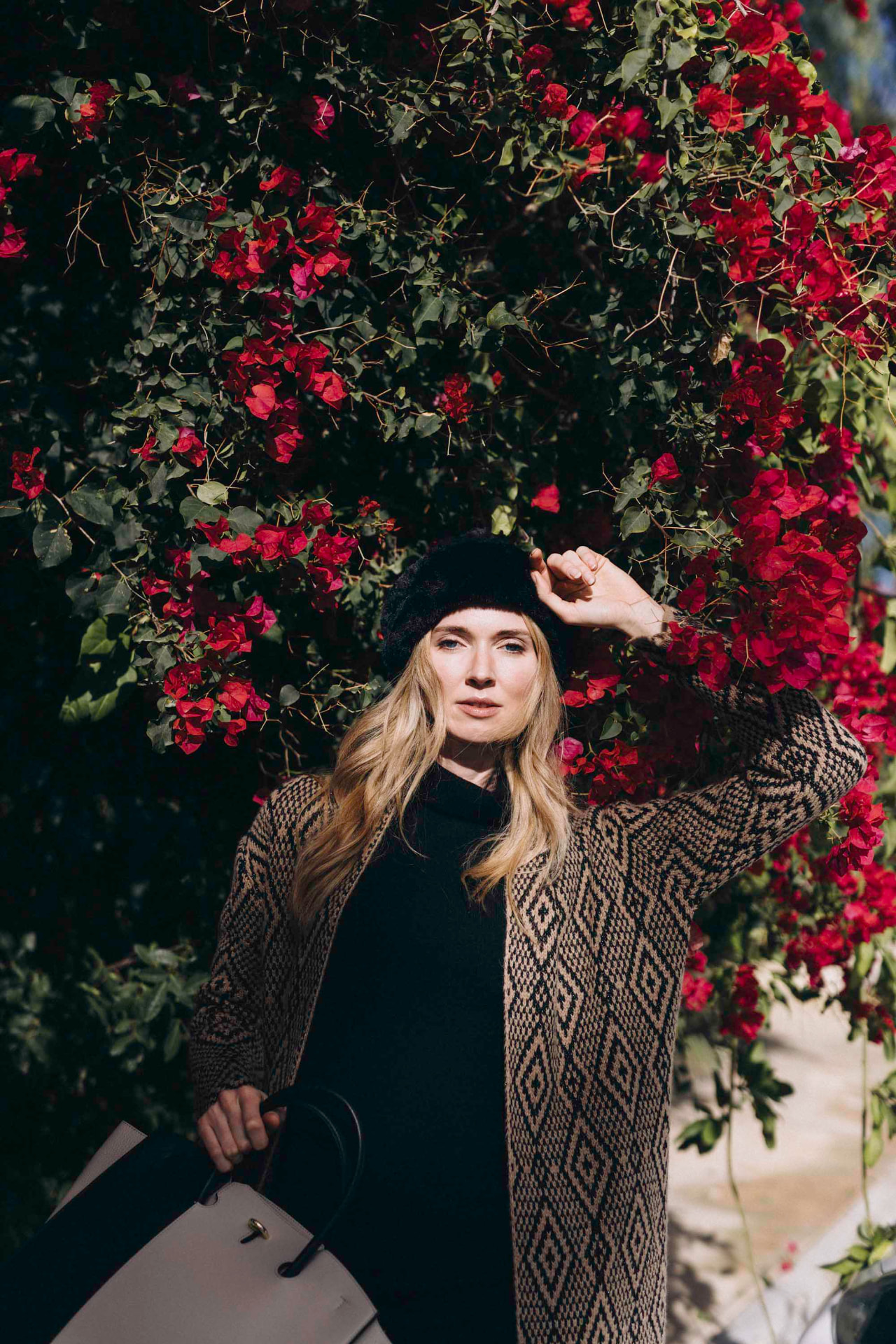 Model in a patterned coat beneath a wall of red bougainvillea