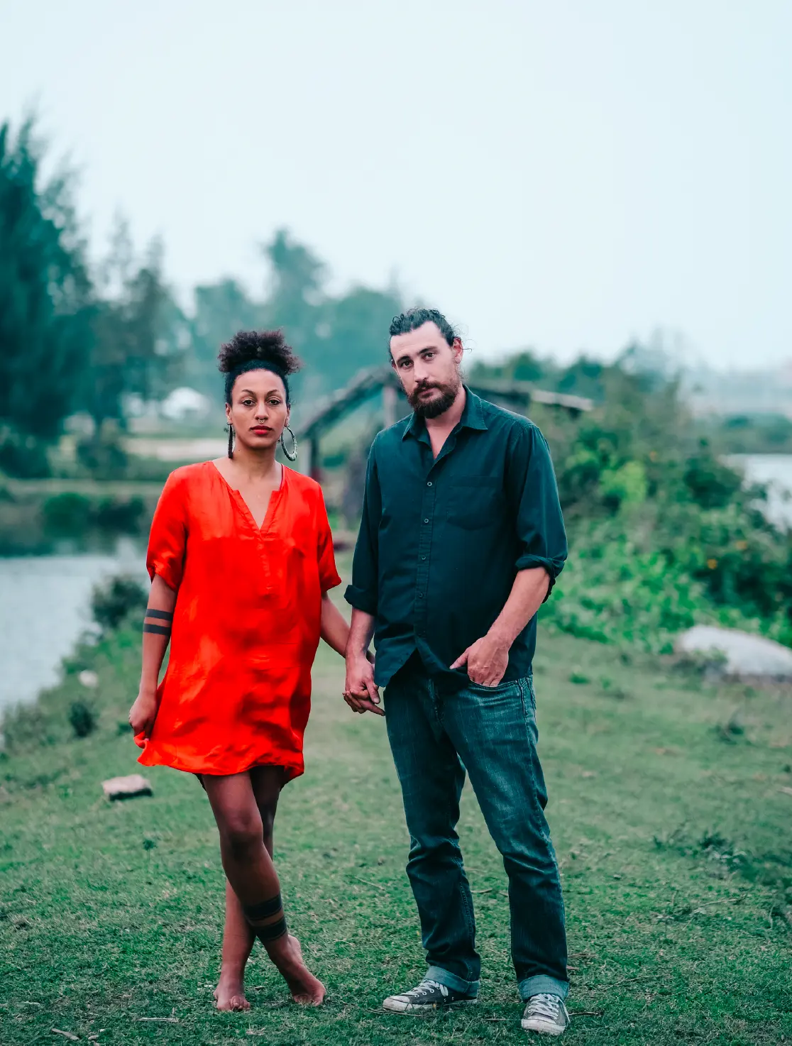 Couple in red and green standing hand in hand by a river