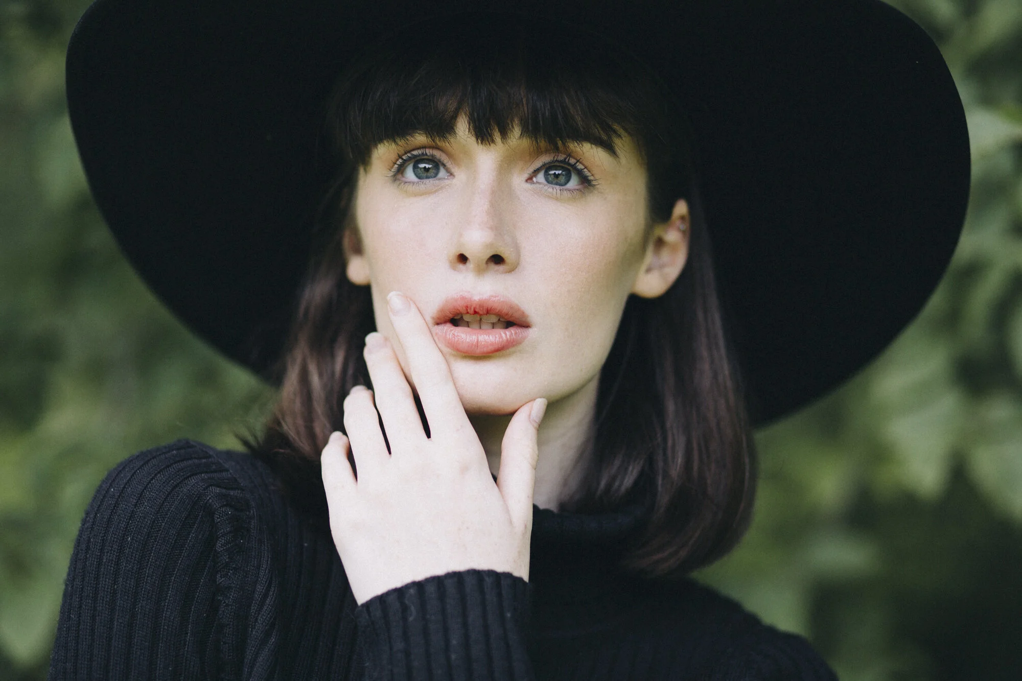 Beauty portrait of a model in a wide black hat against green foliage