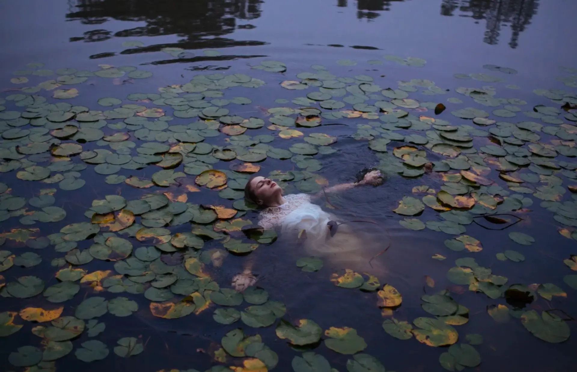 Woman in white lace floating among lily pads at dusk