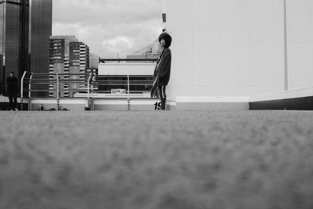 Black and white wide shot of a woman standing on a city rooftop car park