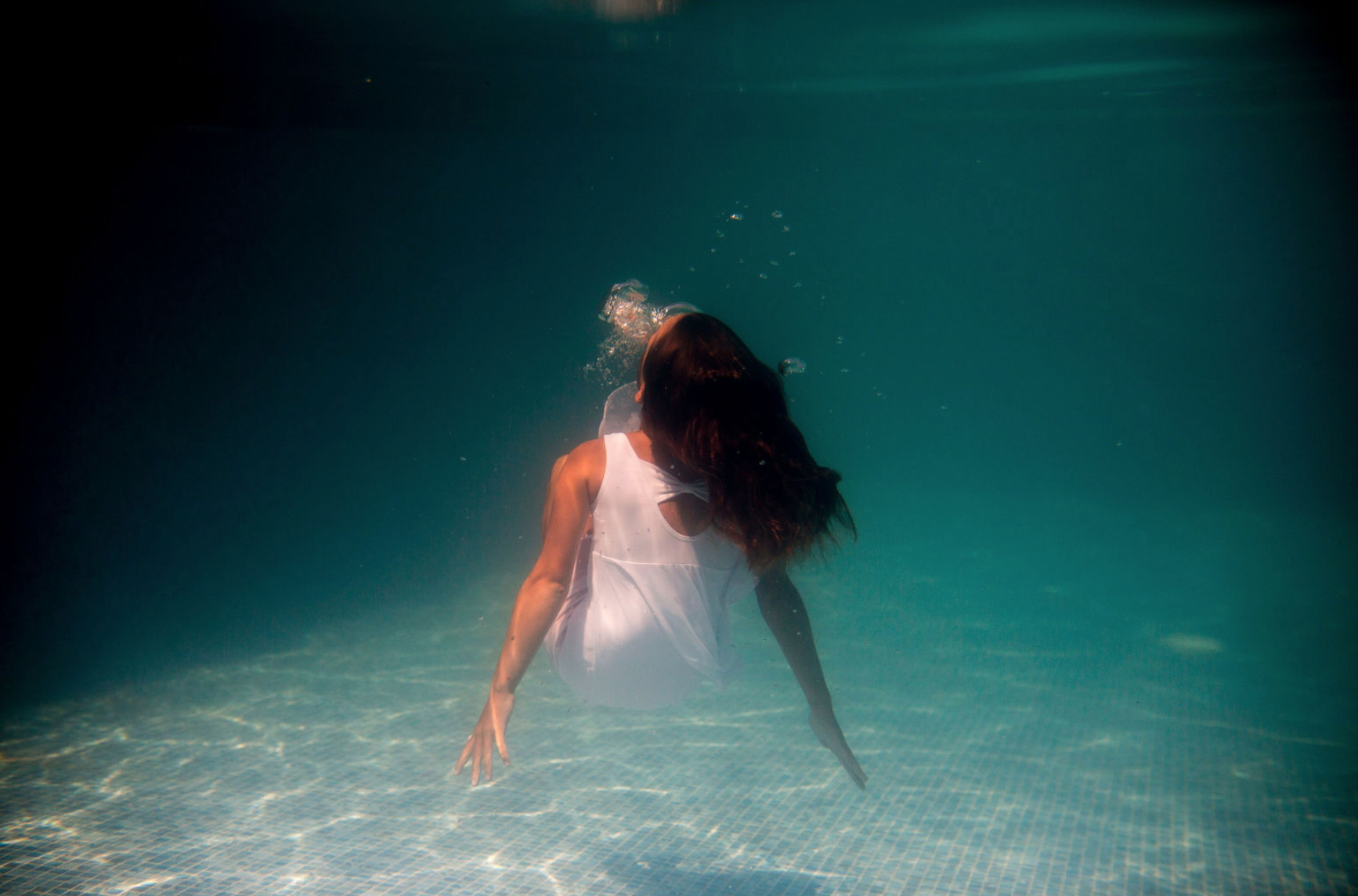 Woman in white swimming away through sunlit turquoise water