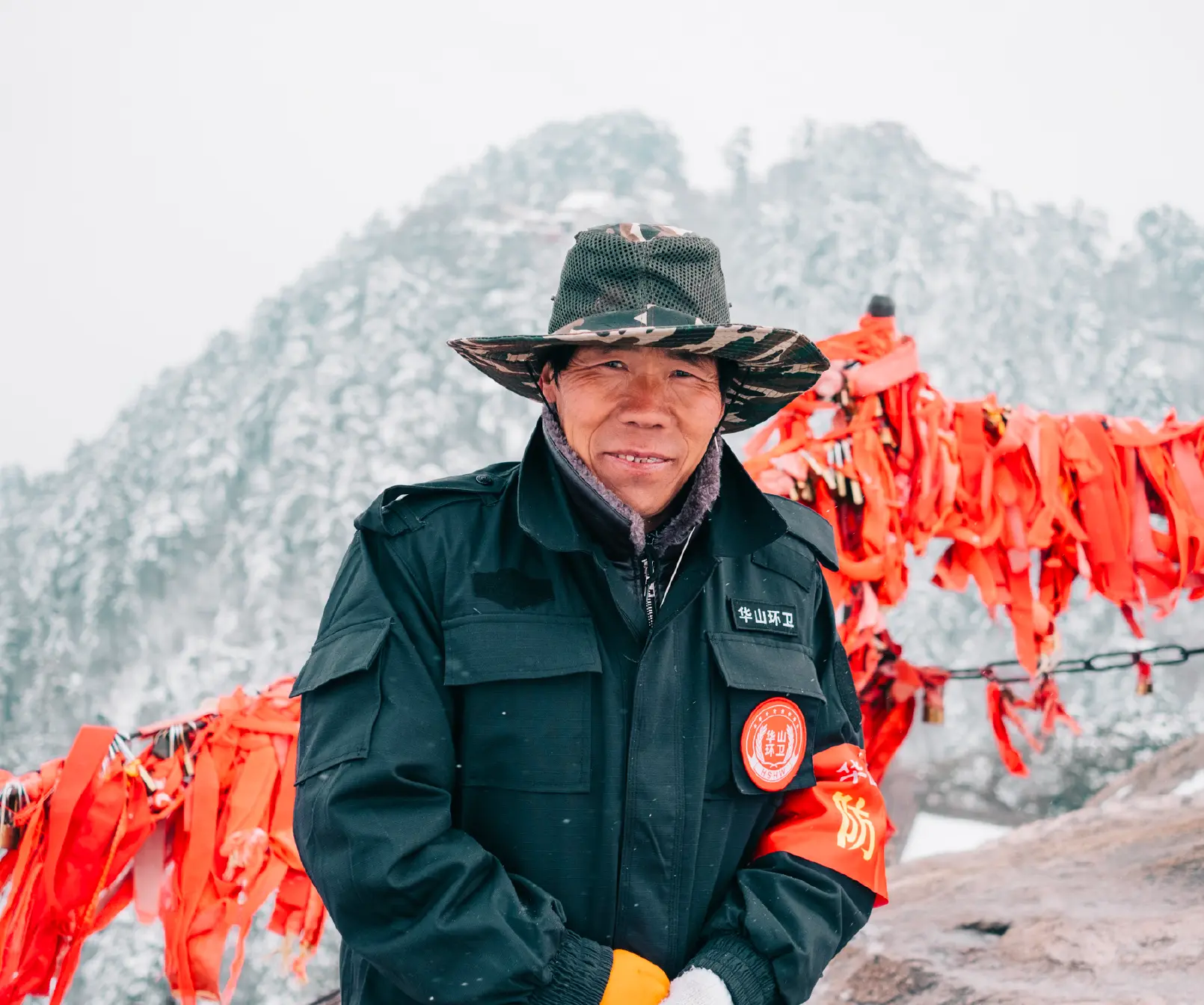 Mountain warden smiling beside red prayer ribbons in the snow on Huashan