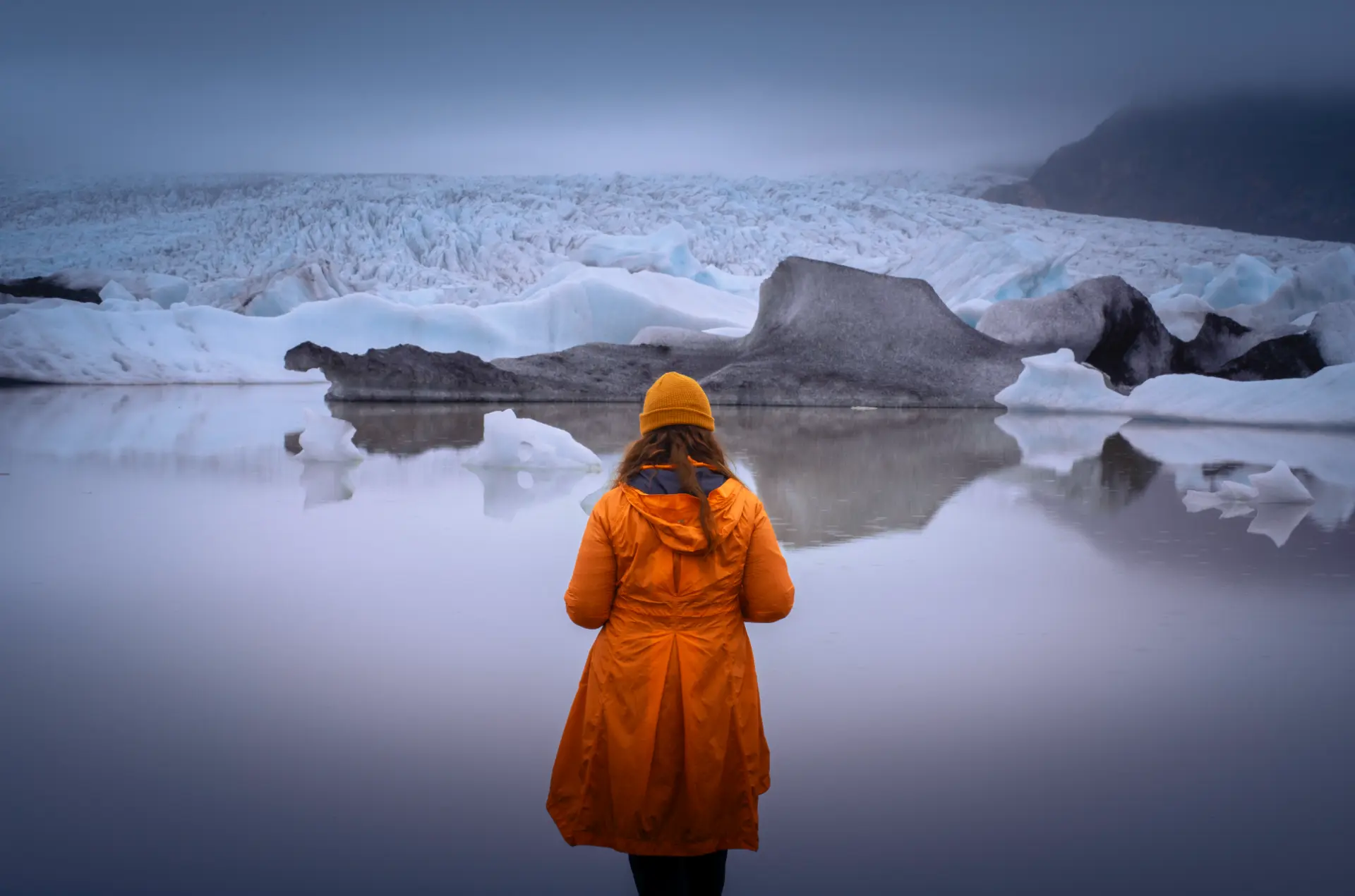 Woman in an orange coat facing a glacier lagoon