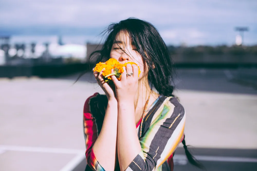 Woman laughing behind a handful of orange marigolds on a rooftop