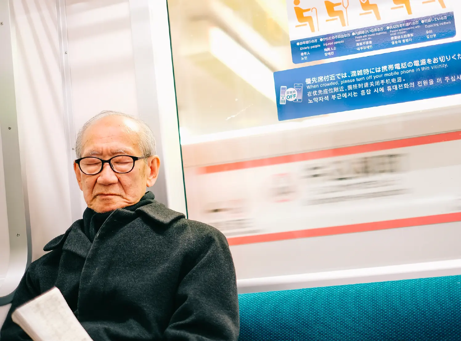 Elderly man asleep with a book on a Tokyo subway train