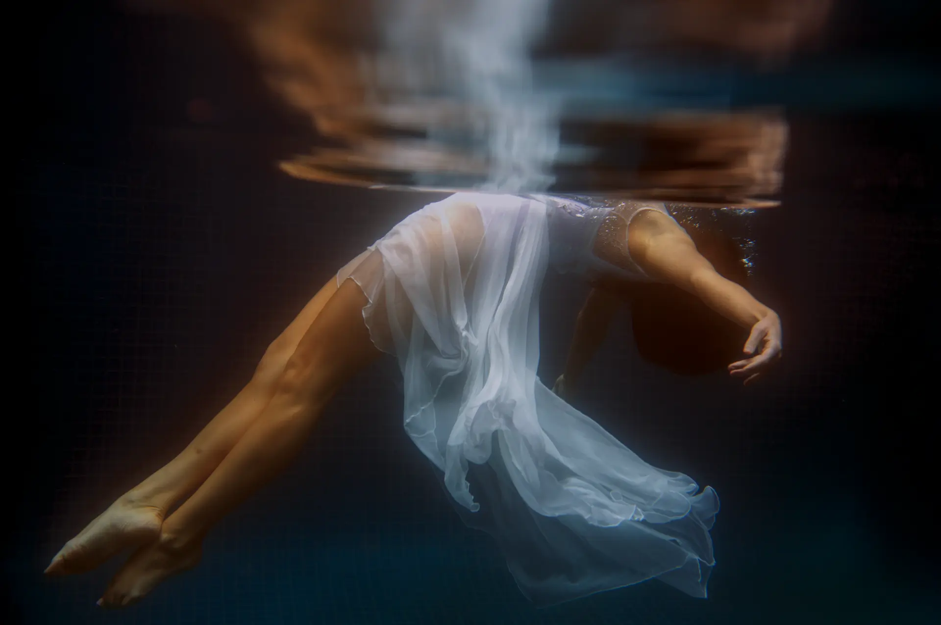Woman in a white dress drifting beneath the surface of a pool