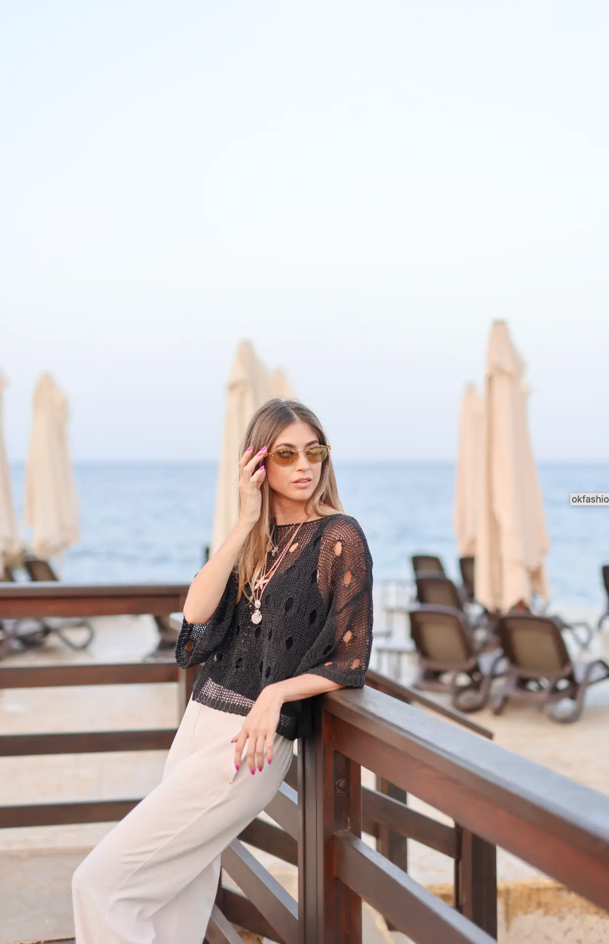 Model in a black crochet top and layered necklaces by the sea
