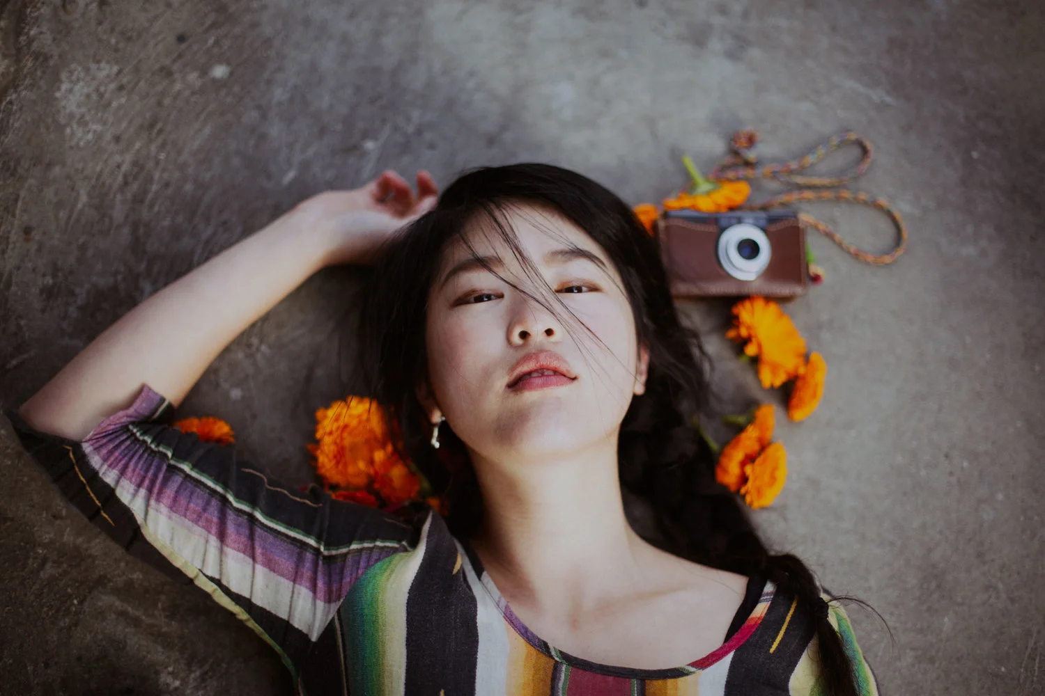 Overhead portrait of a woman lying on concrete beside marigolds and a camera
