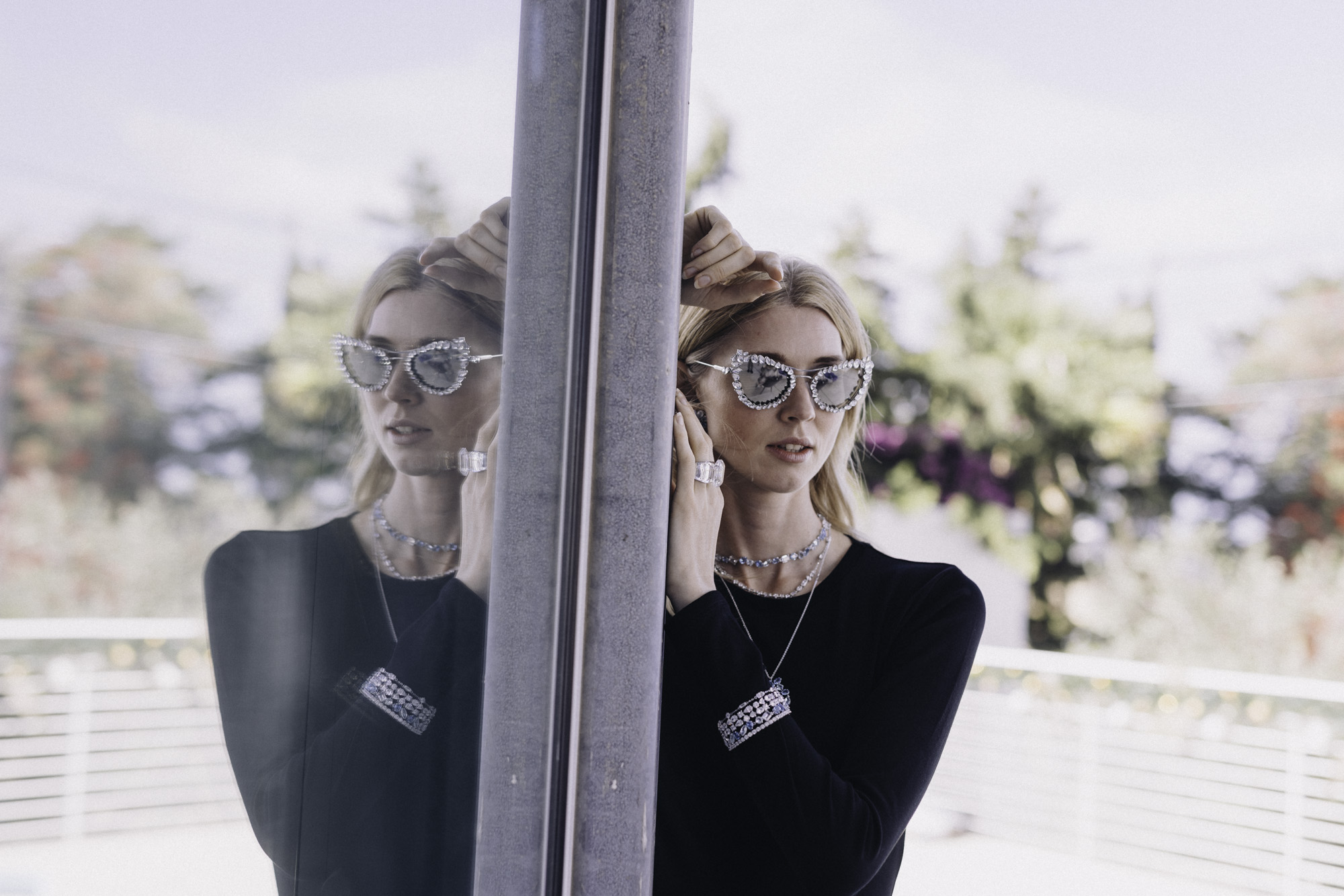 Model reflected in glass wearing sapphire jewellery and jewelled sunglasses