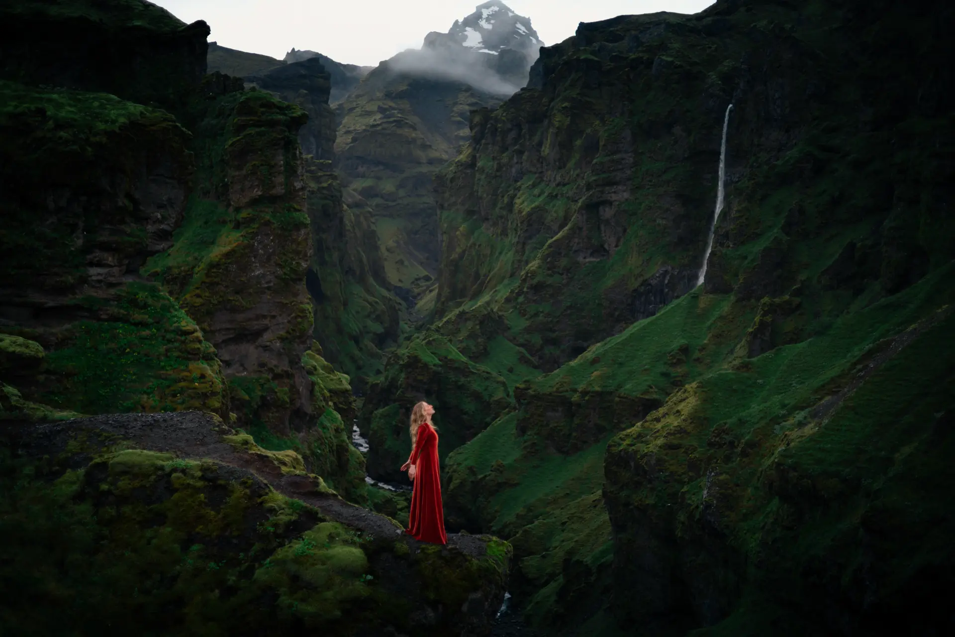 Woman in red velvet before a snow-capped peak in the canyon