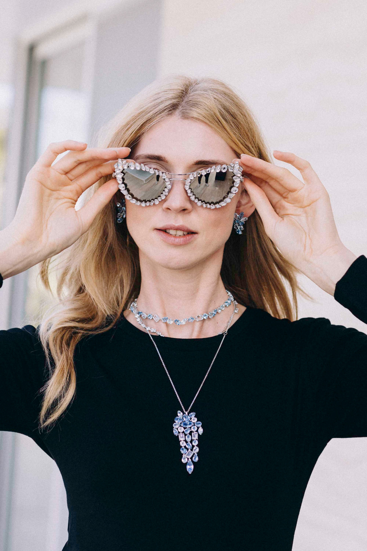 Model lifting crystal-encrusted sunglasses wearing aquamarine jewellery