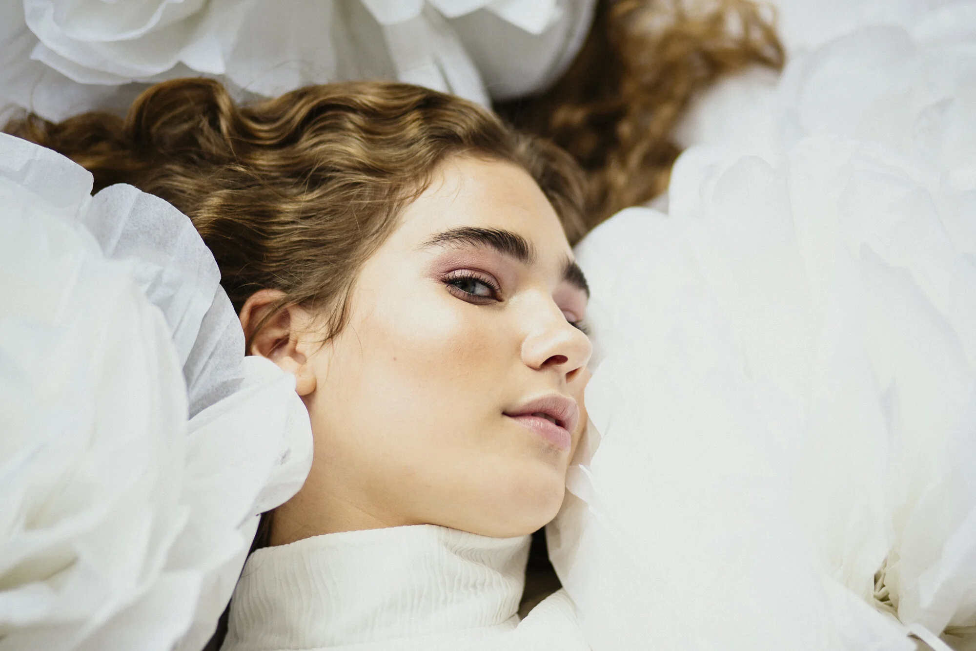 Model lying among oversized white paper flowers