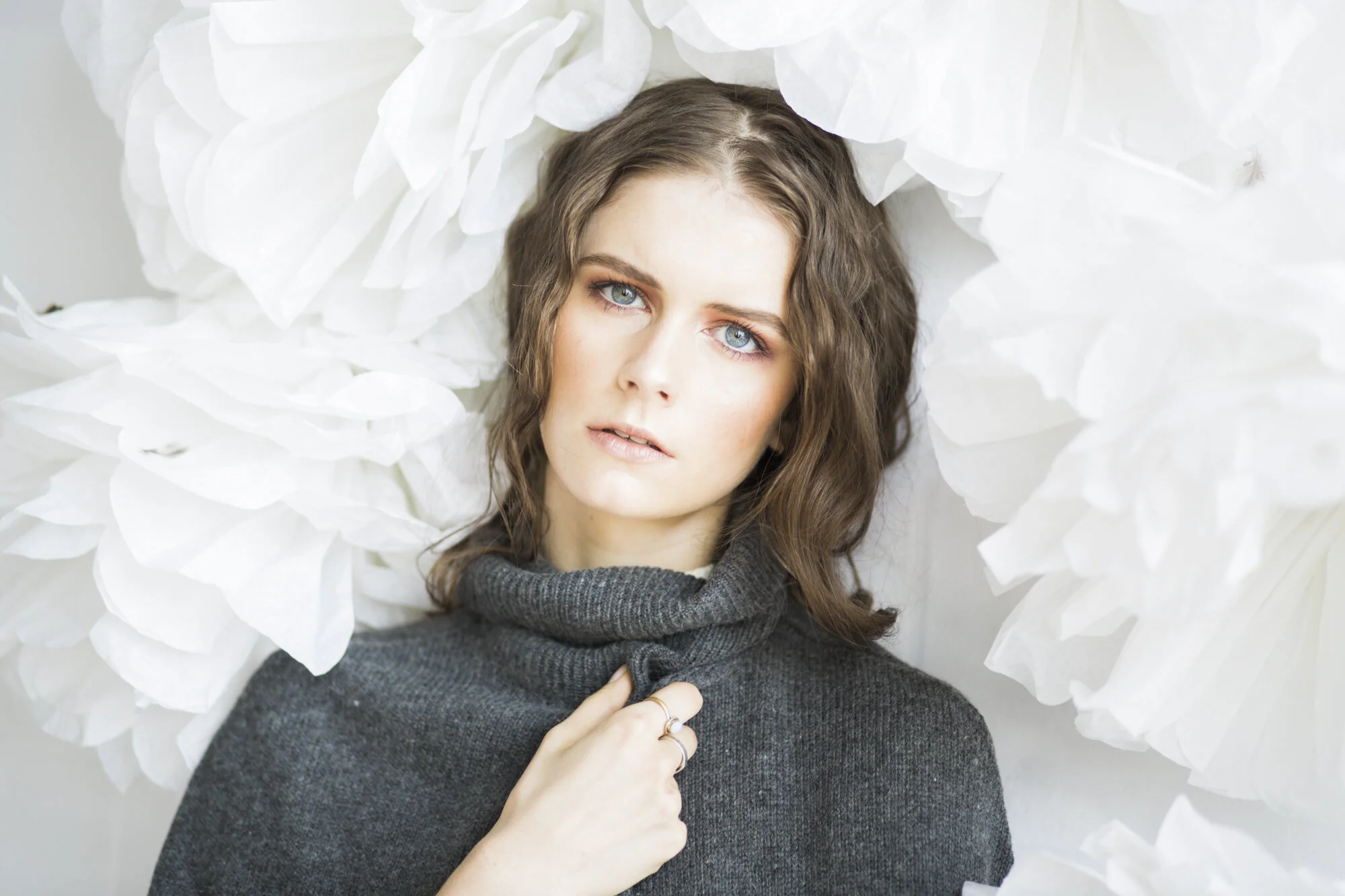 Model in a grey roll-neck against a wall of white paper flowers
