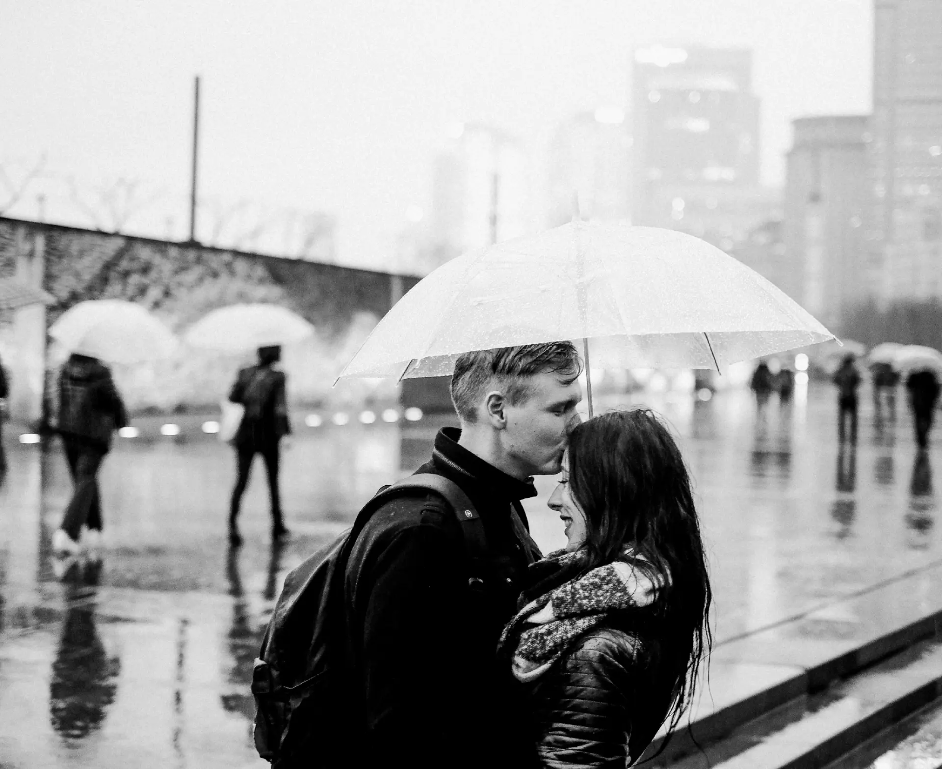 Black and white photograph of a couple under an umbrella in city rain