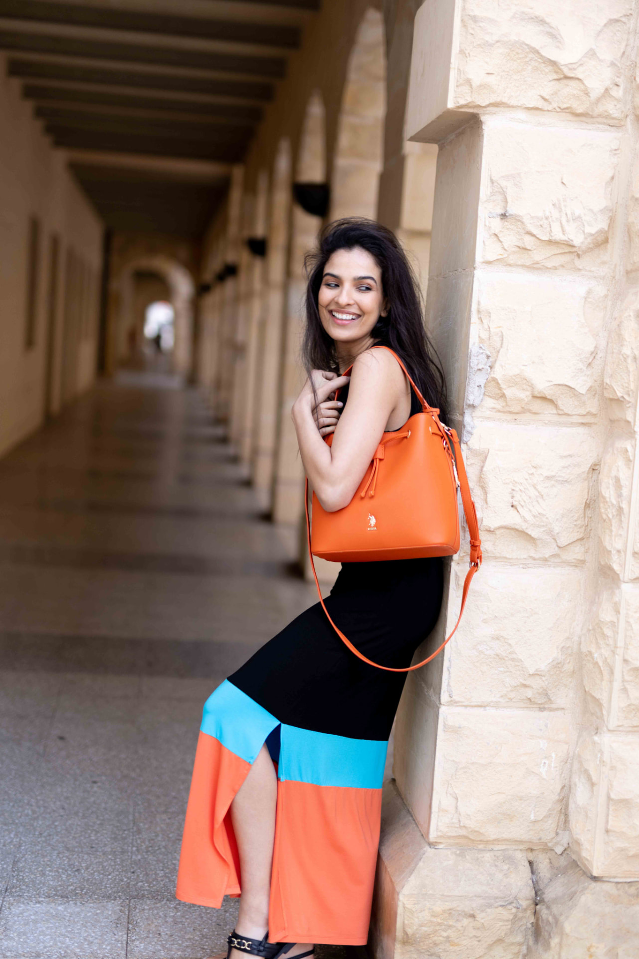 Model with an orange handbag leaning against a limestone colonnade