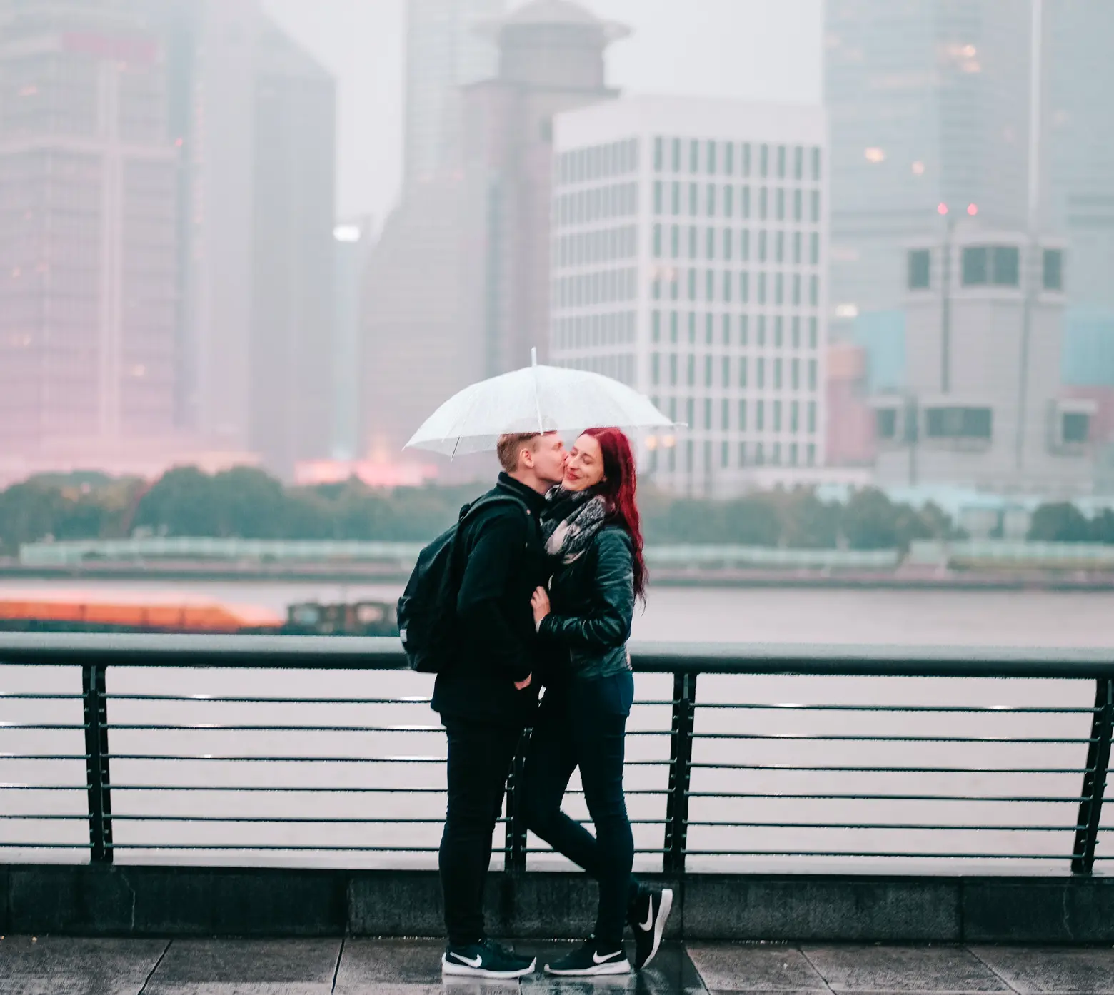 Couple kissing under an umbrella on a misty Shanghai waterfront