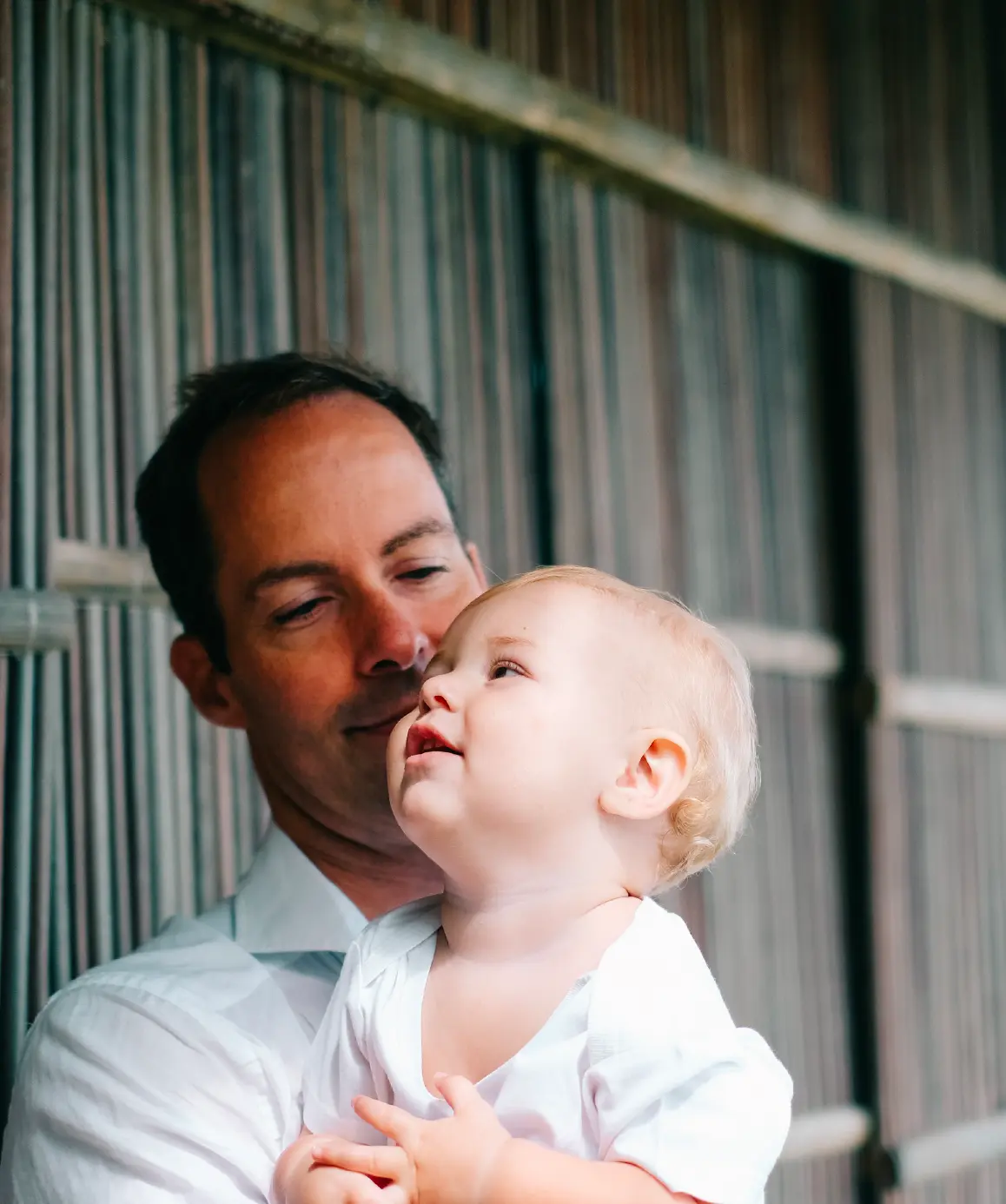 Father holding his fair-haired baby beside a bamboo screen