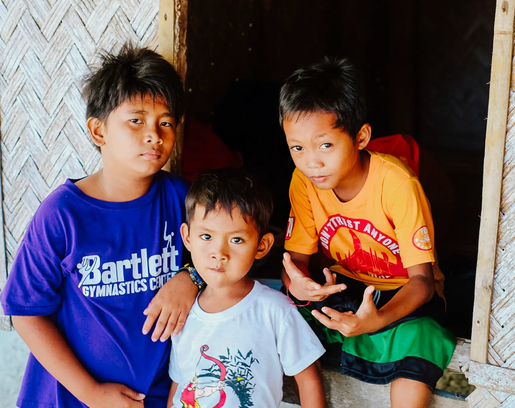 Three brothers in bright t-shirts in the doorway of a bamboo house