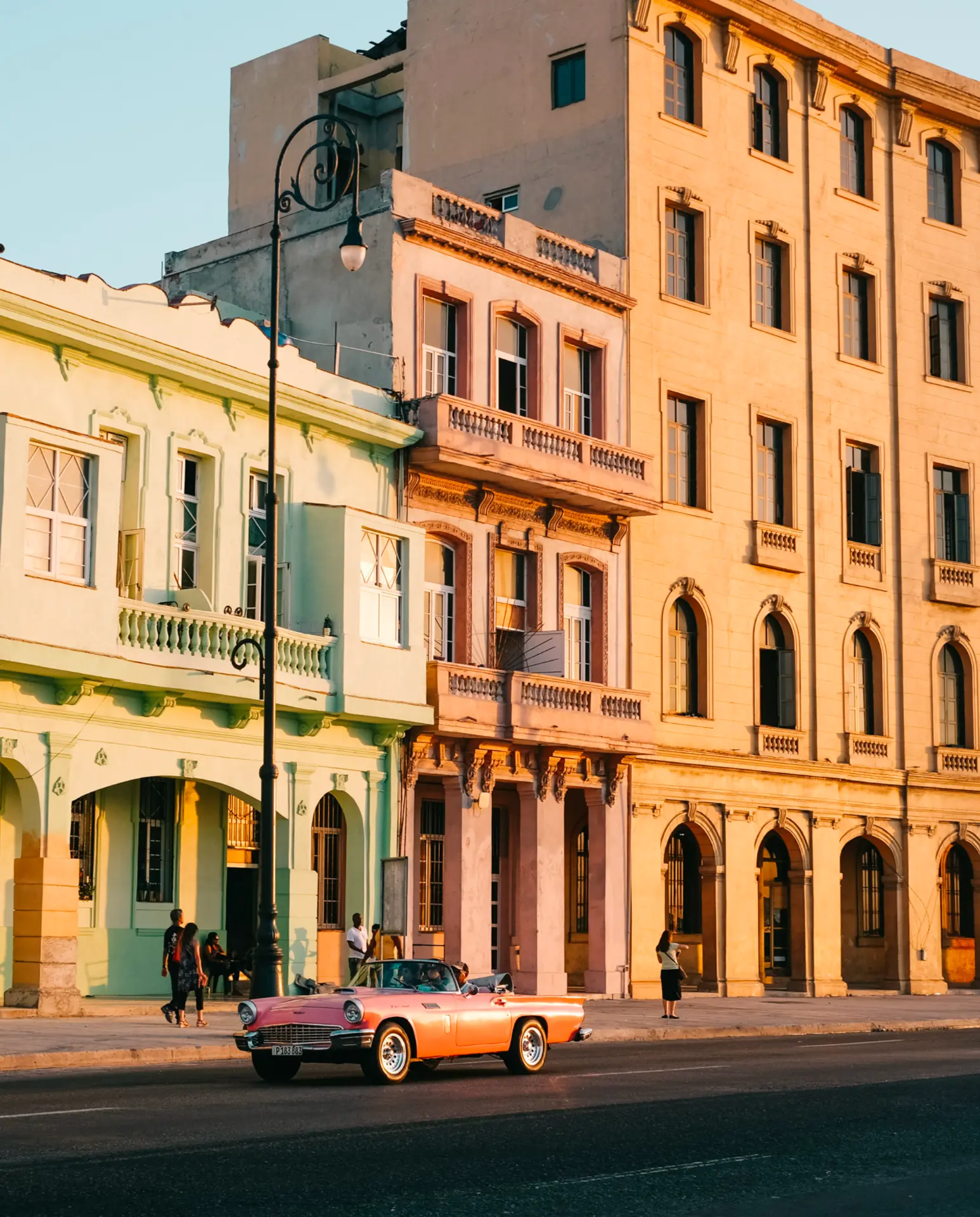 Vintage pink convertible passing pastel colonial facades in Havana at sunset