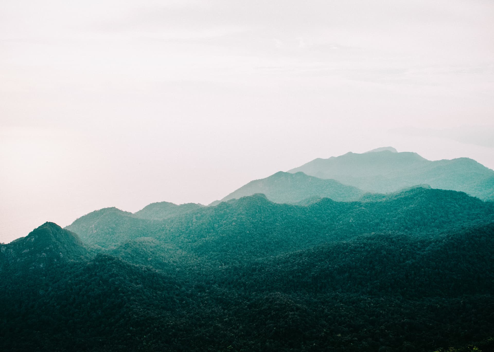 Layered misty green mountain ridges fading into pale sky