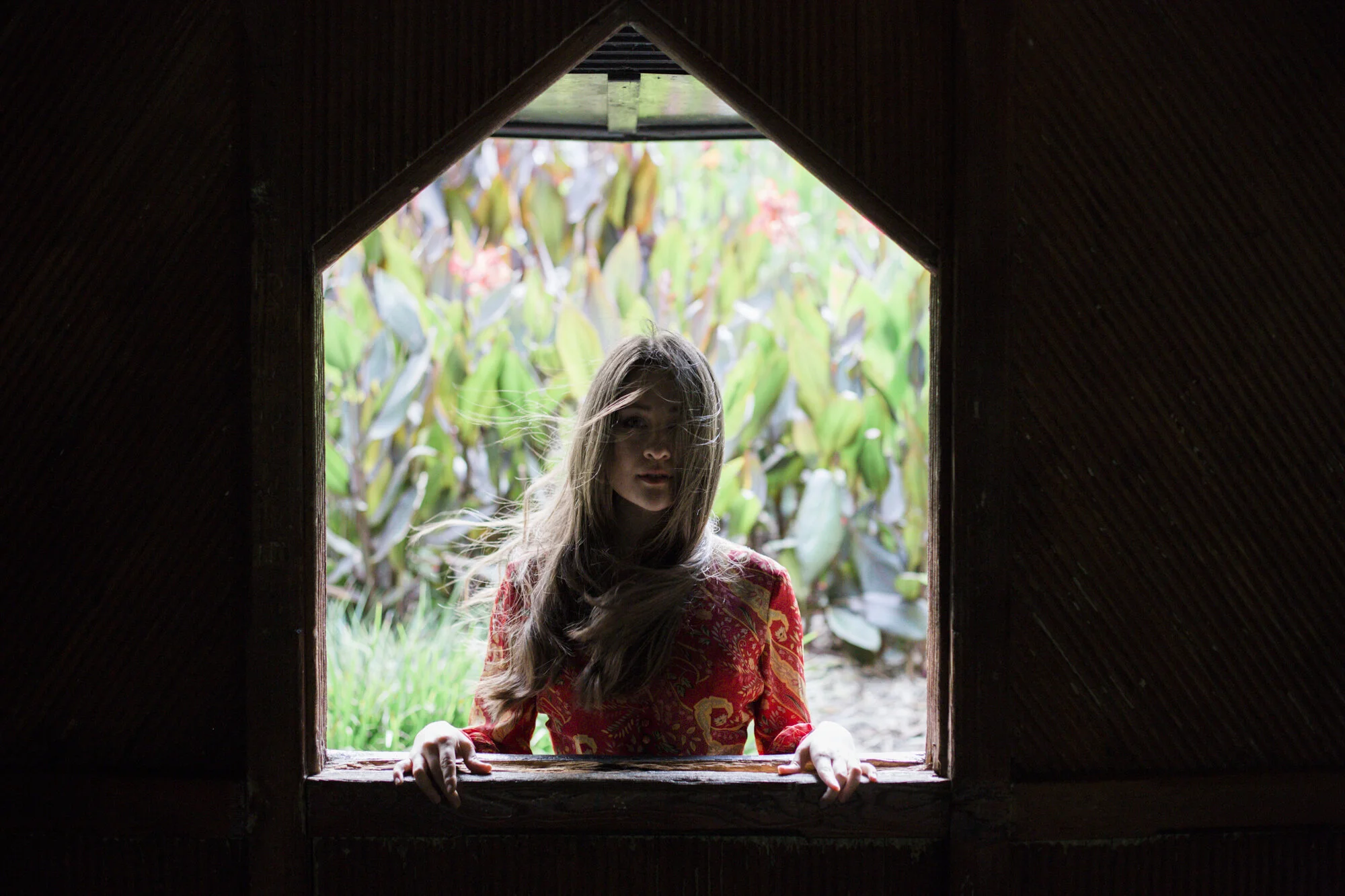 Woman in a red floral dress framed in a dark wooden garden window