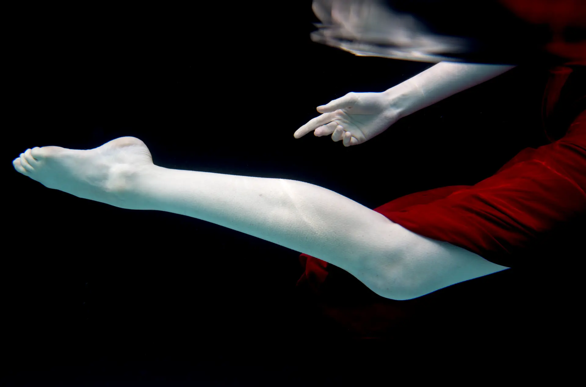 Underwater study of a figure in red silk, limbs suspended in dark water
