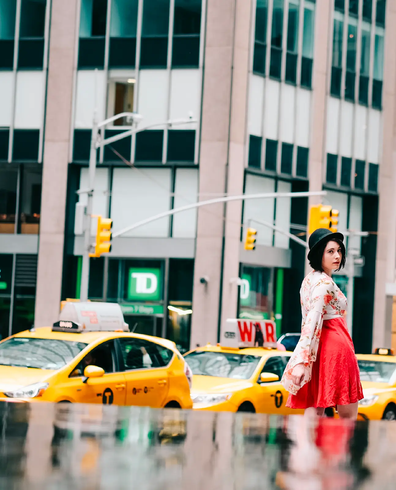 Woman in a red skirt turning beside yellow cabs on a New York street