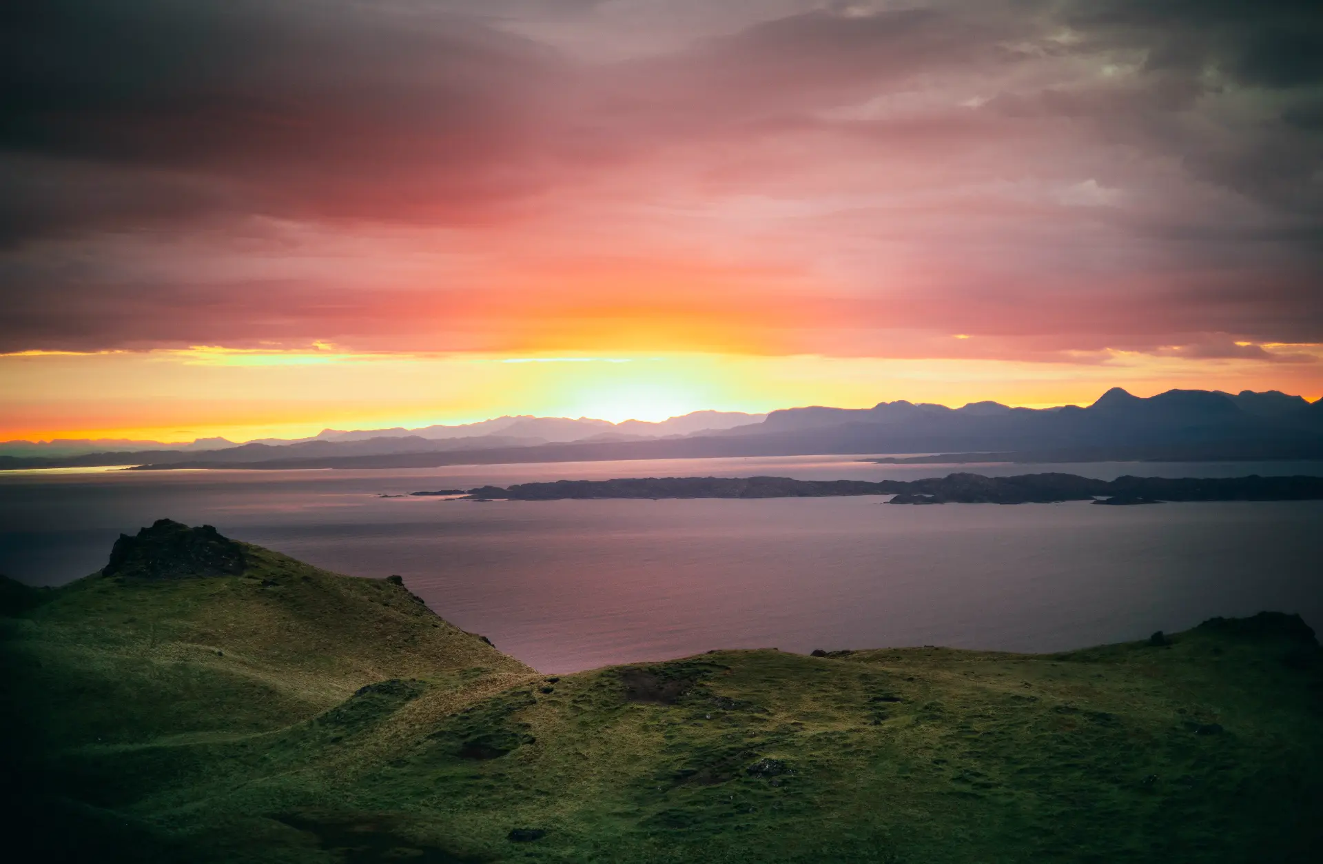 Fiery sunset over sea lochs and distant mountains from a grassy Skye ridge
