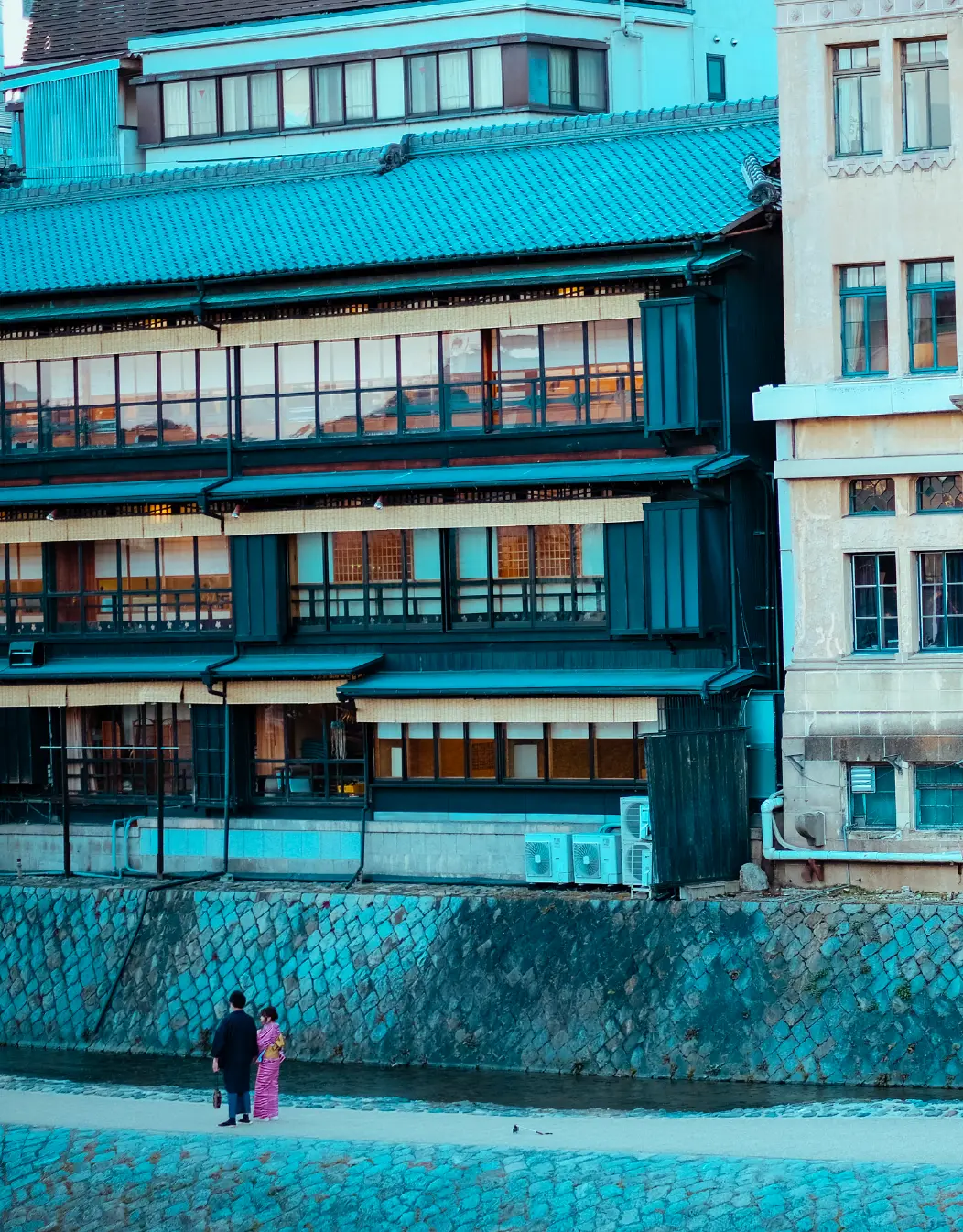 Couple in kimono walking the Kamo river beneath a Kyoto teahouse