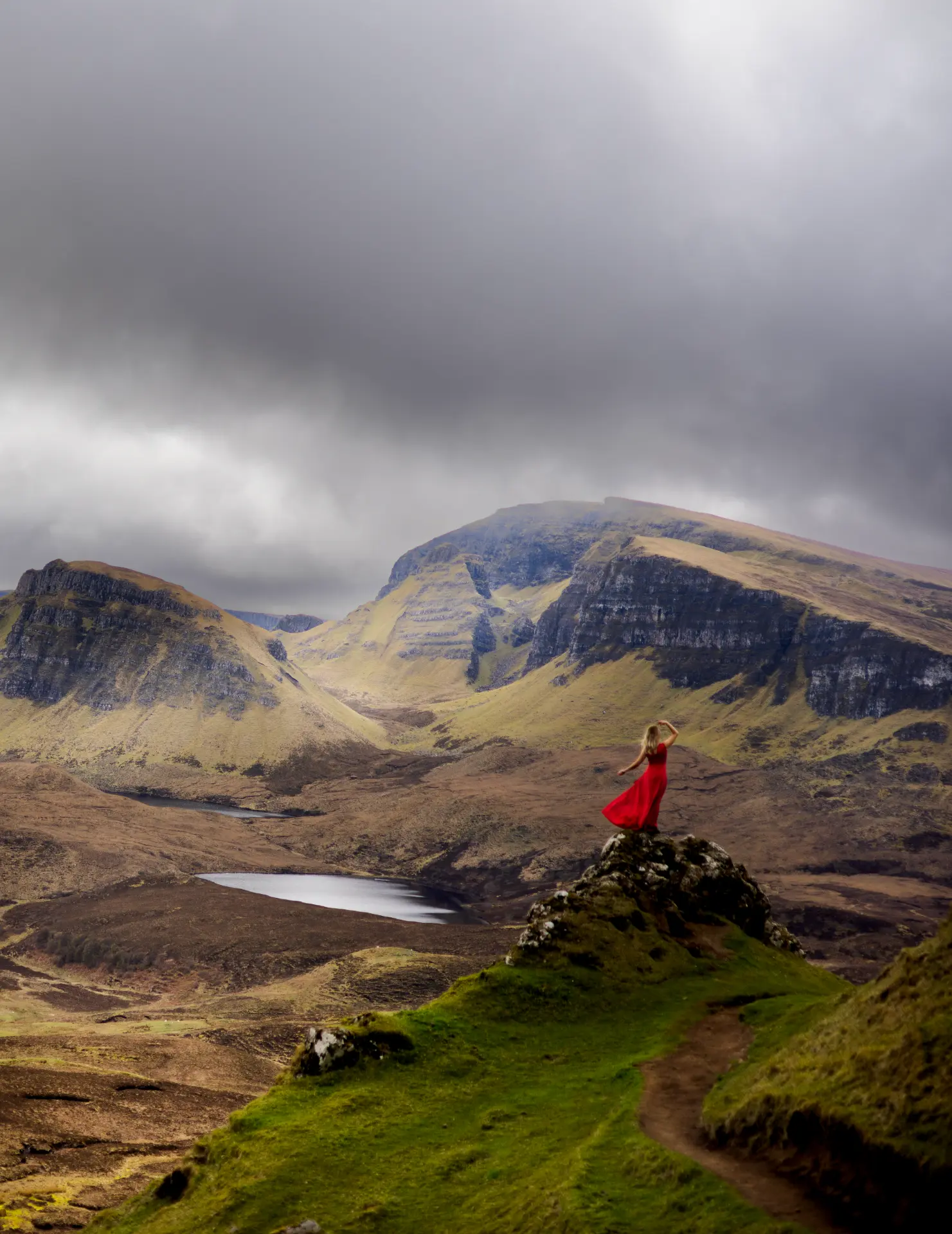 Woman in a flowing red dress overlooking the Quiraing landscape