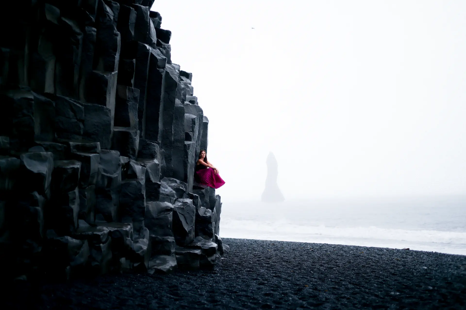 Woman in magenta resting on the basalt columns of Reynisfjara black sand beach