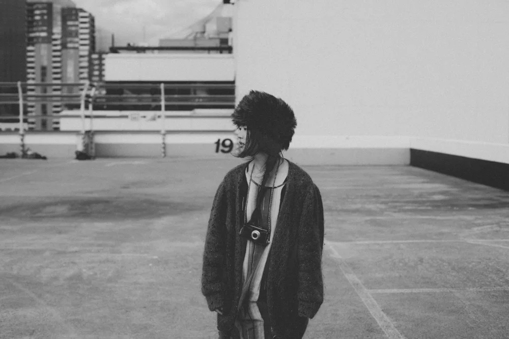 Black and white portrait of a woman in a fur hat with a film camera on a rooftop